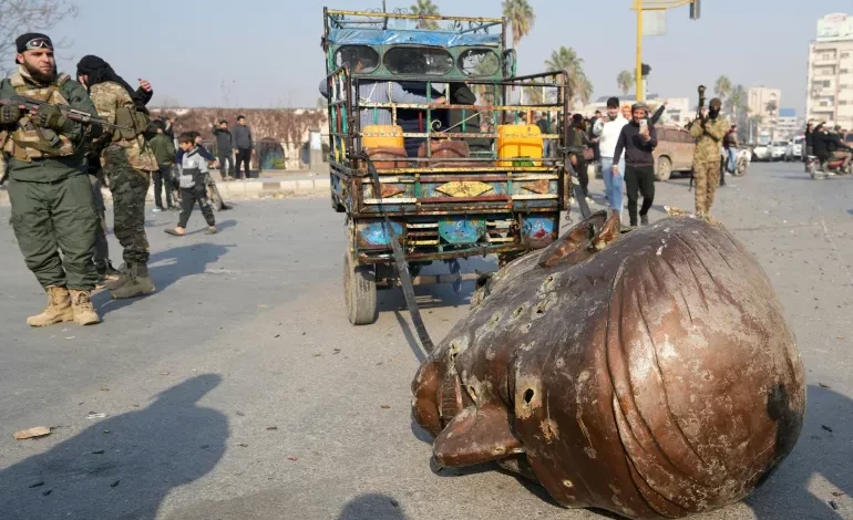 مقاتل من المعارضة المسلحة يقف بجانب تمثال محطم لحافظ الأسد (الفرنسية)